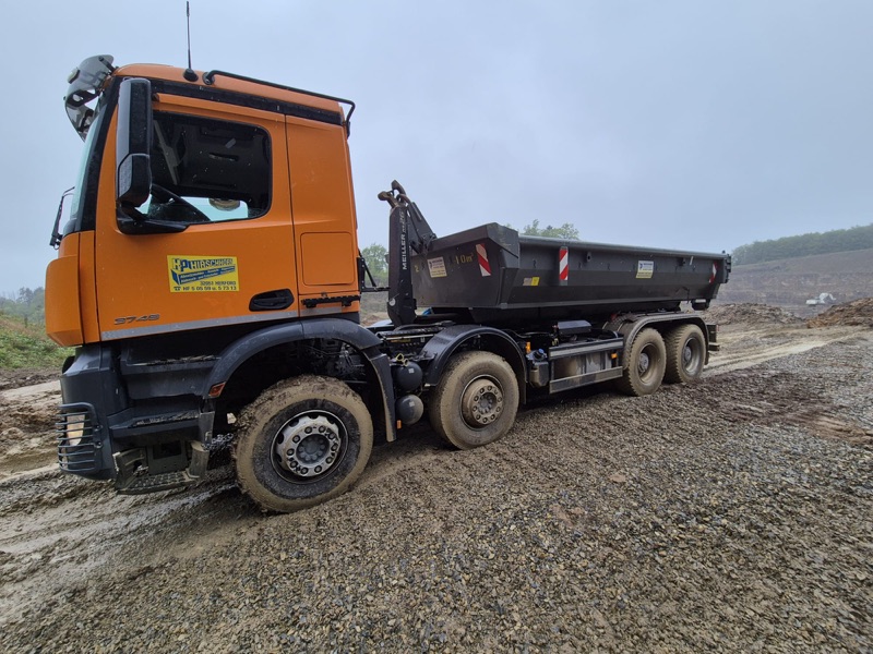 Orangefarbener Hirschhorn-Kipper mit 10-m³-Abrollcontainer auf einer Baustelle bei Herford