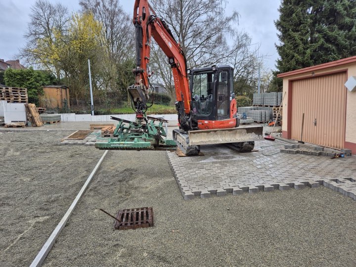 Minibagger mit Verlegegerät verlegt Betonpflaster auf einem Hof in Herford